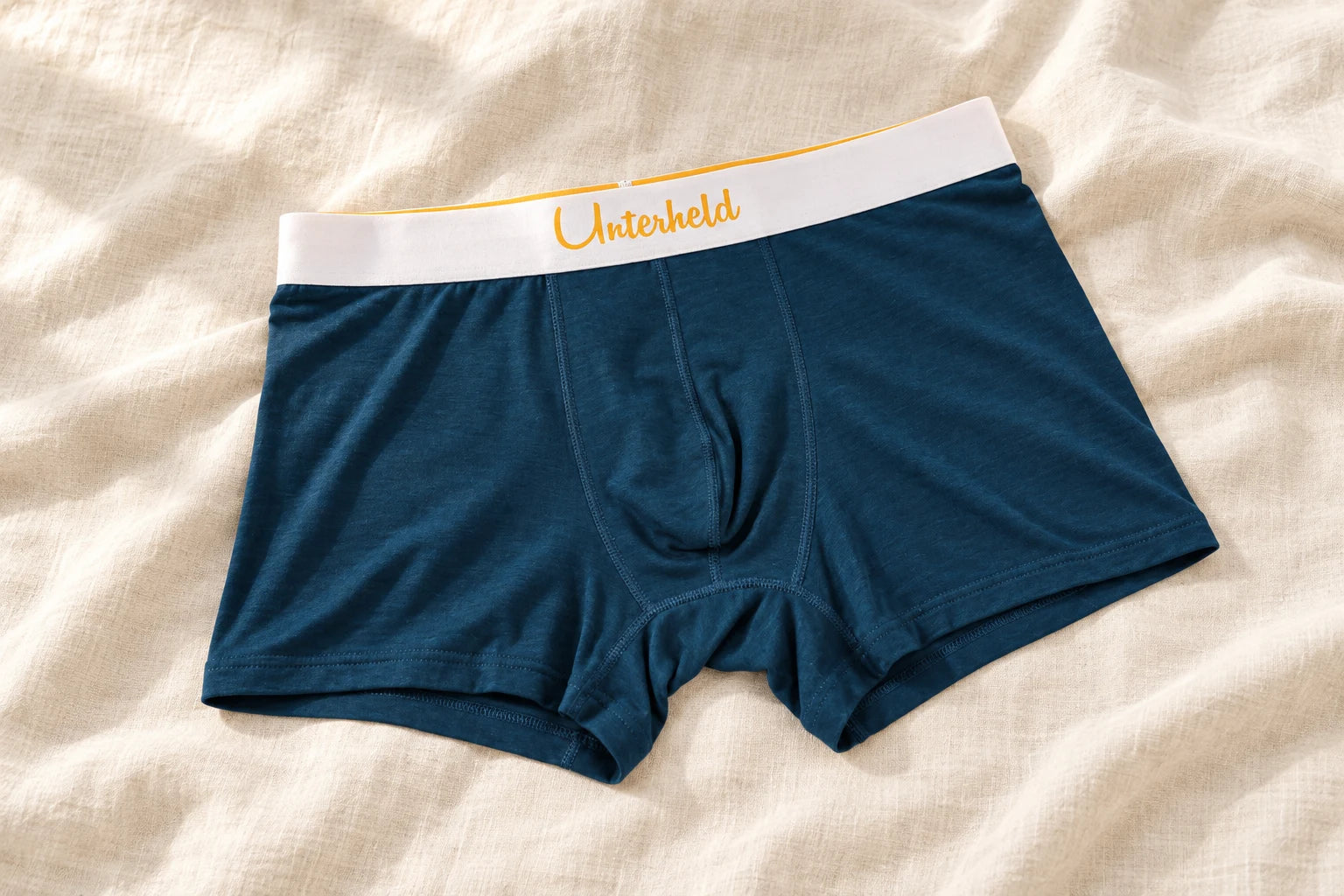 Dunkelblaue Unterheld Boxershorts auf hellem Leinen mit goldenem Unterheld Schriftzug am weißen Bund